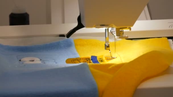 Η βελόνα της ραπτομηχανής για κέντημα κάνει ένα στολίδι σε ένα κομμάτι μπλε και κίτρινο ύφασμα. Ειδική ραπτομηχανή για κεντήματα στη δουλειά. Προγραμματιζόμενη ραπτομηχανή - Πλάνα, βίντεο