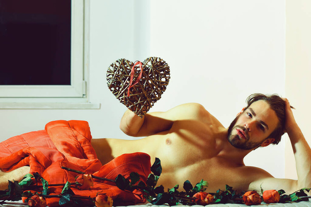 bearded macho man with velentine on bed under red blanket around orange roses - Photo, Image