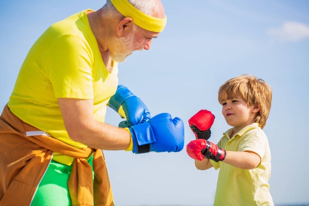 A kisfiú bokszolt a nagyapjával. Apa bokszolni tanítja a fiát. Kisfiú sportoló a boksz edzésen az edzővel - Fotó, kép