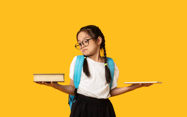 Зіткнулася з японською школяркою Порівнюючи планшет і книгу за жовтим фоном - Фото, зображення