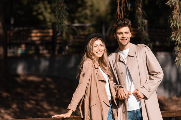stylish man in trench coat holding hands with woman in hat  - Photo, Image