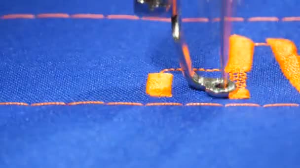 Uma agulha especial de uma máquina de costura bordar letras laranja em tecido azul em uma loja de alfaiate ou oficina de costura vista de perto - Filmagem, Vídeo