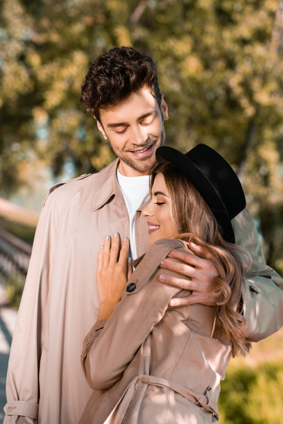 hombre en gabardina abrazando a mujer en sombrero afuera - Foto, imagen