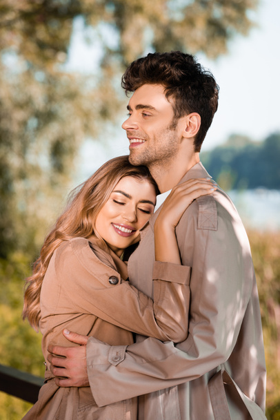 woman with closed eyes hugging man in trench coat outside - Foto, imagen