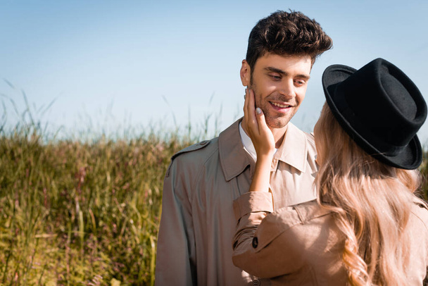 blonde woman in hat touching face of man in trench coat  - Foto, afbeelding