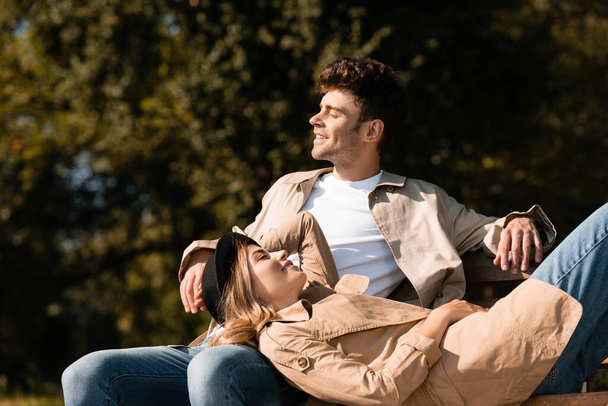 rubia mujer en sombrero acostado en el hombre sentado en el banco en el parque - Foto, Imagen