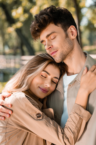 girlfriend hugging boyfriend with closed eyes in autumnal park  - Фото, изображение