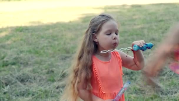 Cute little girl with long hair blows bubbles. Happy child. - Imágenes, Vídeo