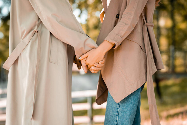 partial view of man and woman in trench coats holding hands in park - Foto, imagen