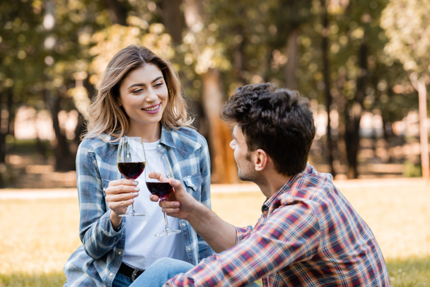 man and woman holding holding glasses with red wine in park - Photo, Image