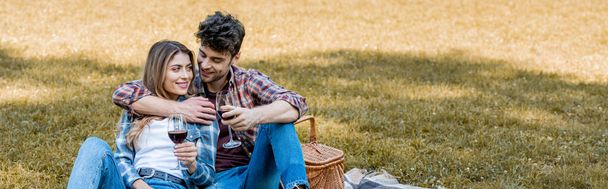 horizontaal beeld van man en vrouw met glazen met rode wijn tijdens de picknick  - Foto, afbeelding