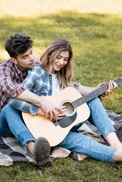 woman sitting on blanket and playing acoustic guitar with boyfriend  - Fotó, kép