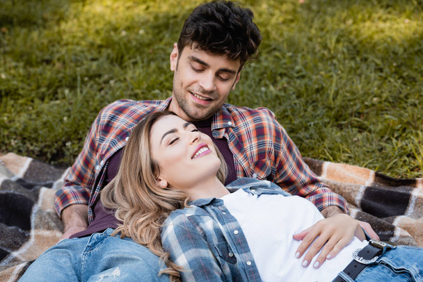 man looking at woman in plaid shirt lying on blanket  - Photo, Image