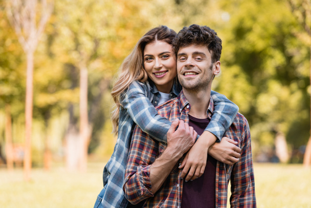 woman embracing man in checkered shirt in park - Photo, Image