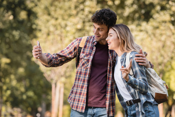 mężczyzna biorąc selfie z kobieta pokazując znak pokoju w jesiennym parku - Zdjęcie, obraz