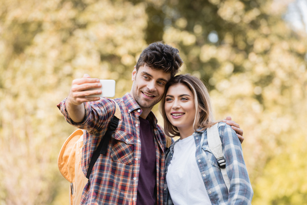 joyful man and woman taking selfie in autumnal park - Photo, Image