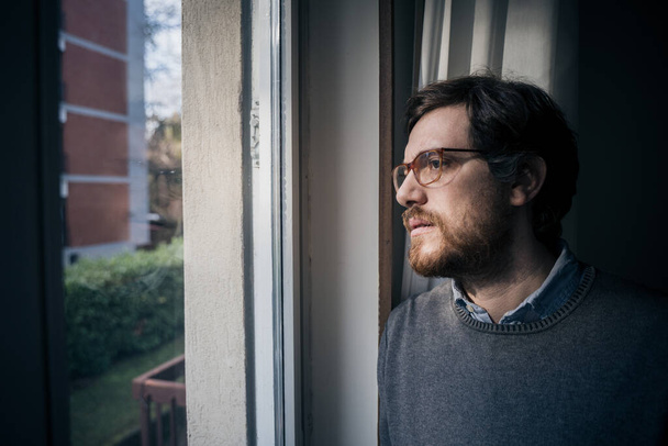 Portrait of one guy longing and looking through window - Photo, Image