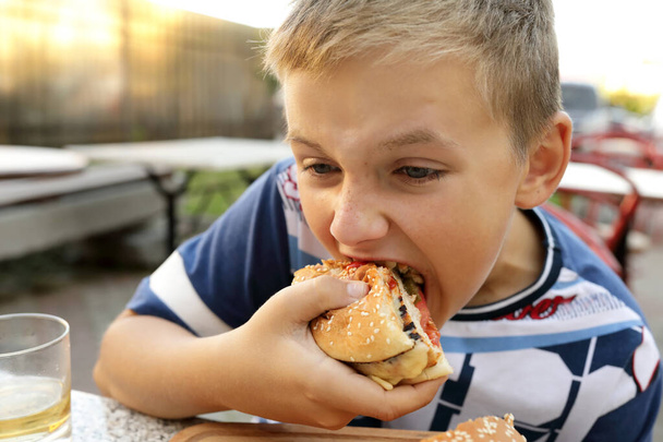 Boy eating burger in an outdoor restaurant - Фото, изображение