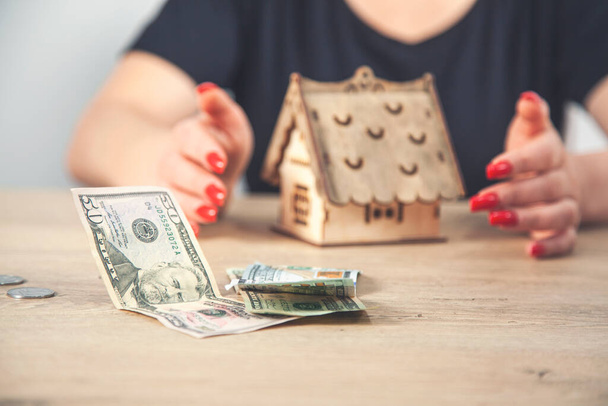 Saving money for house and real estate. Woman hand protecting on stack coins and house model on table - Photo, Image