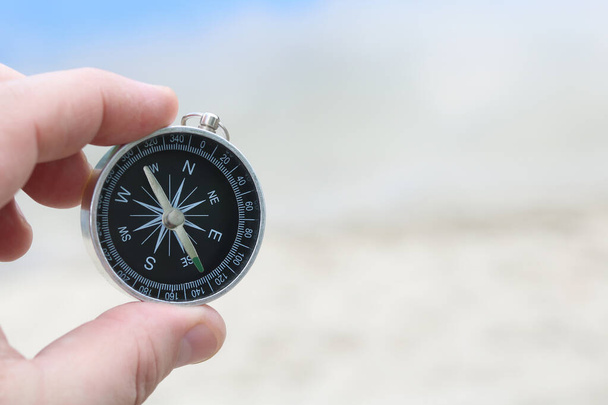 Классический компас в руке на фоне песчаного пляжа и синего моря как символ туризма с компасом, путешествия с компасом и активного отдыха с компасом - Фото, изображение