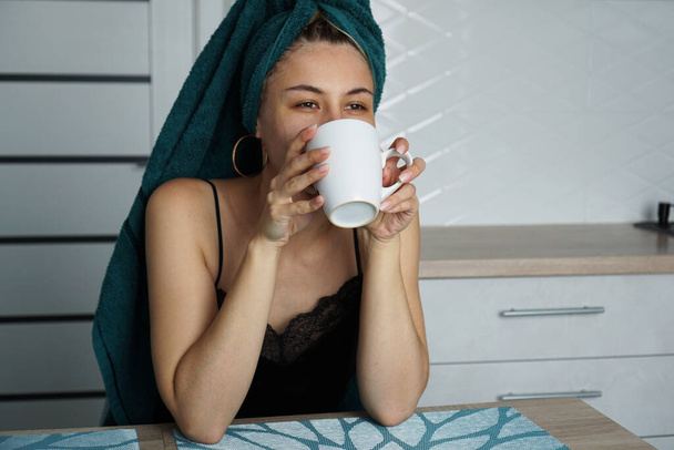 Beautiful woman sits in the kitchen with a cup of coffee - Foto, afbeelding