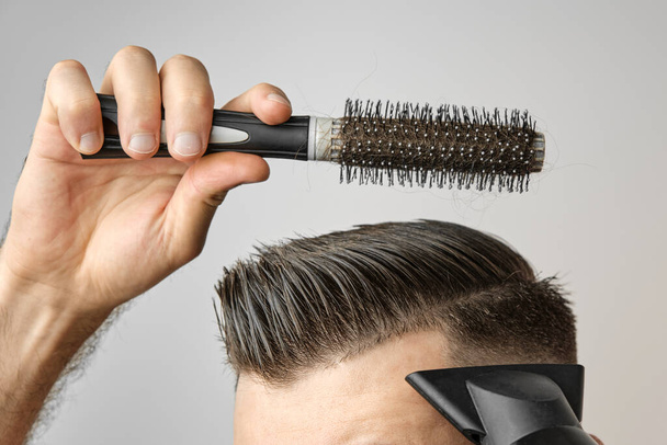 Muž stylizující si vlasy vysoušečem vlasů a kulatým štětcem. Péče o vlasy doma po holičství. Mans móda a moderní sestřih. - Fotografie, Obrázek