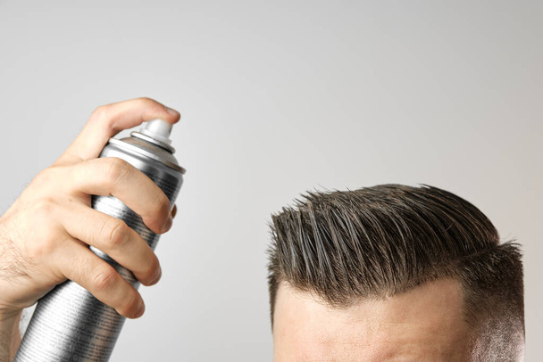 Ο άνθρωπος που εφαρμόζει σπρέι μαλλιών για το χτένισμα των μαλλιών του μετά το κούρεμα του κουρείου. Διαφήμιση έννοια των προϊόντων mans. Θεραπεία και φροντίδα κατά της απώλειας των μαλλιών - Φωτογραφία, εικόνα