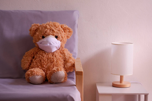 Teddy orso rappresentante di un bambino che indossa una maschera facciale siede sul divano nel soggiorno solitudine e tristezza. Coronavirus Covid-19 e pm2.5, rimanere a casa, concetto di quarantena. - Foto, immagini
