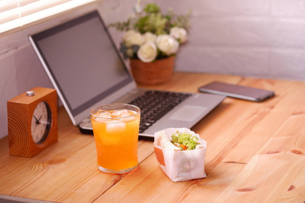 Jedz kanapki i sok pomarańczowy. Podczas pracy z laptopem. Praca i jedzenie w tym samym czasie. Praca w domu. - Zdjęcie, obraz