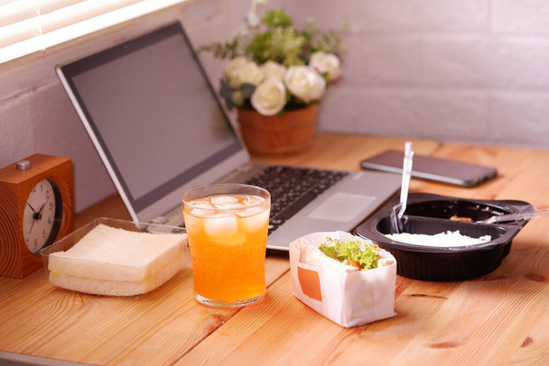 Jedz kanapki i Meal plastikowe pudełko z sokiem pomarańczowym. Podczas pracy z laptopem. Praca i jedzenie w tym samym czasie. Praca w domu. - Zdjęcie, obraz