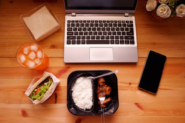 Coma sándwich y Coma una caja de plástico con jugo de naranja. Durante el trabajo con el ordenador portátil. Trabajar y comer alimentos al mismo tiempo. Trabajo en casa. - Foto, imagen