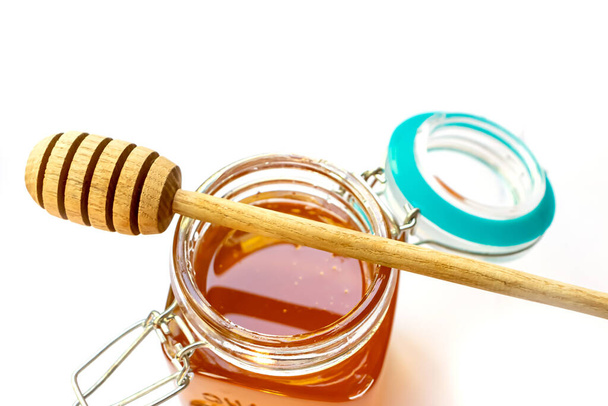 Cuillère à miel en bois posée sur un bocal en verre ouvert avec du miel doré floral - Photo, image