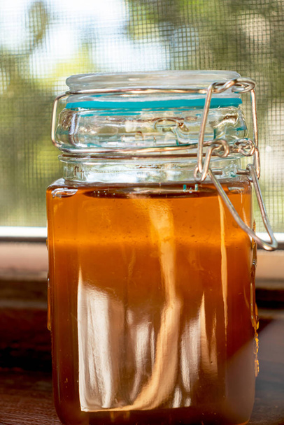 Ein Glas mit einem Deckel, gefüllt mit goldenem Honig. Grün im Hintergrund - Foto, Bild