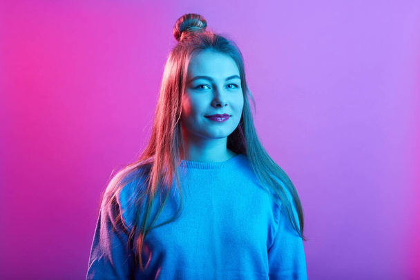 Attractive lady standing isolated over pink neon background and looking directly at camera, expressing positive emotions, wearing casual sweater. - Valokuva, kuva