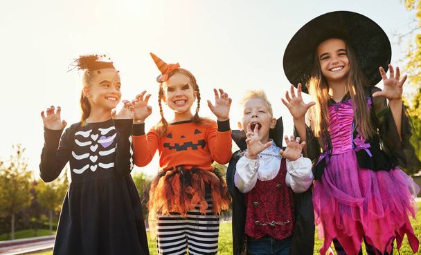 Groep kinderen in Halloween kostuums gebarentaal en het maken van enge gezichten tegen wolkenloze lucht in par - Foto, afbeelding