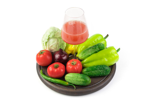 Een grote selectie groenten en een glas vers geperst groentesap op een rond dienblad op een witte achtergrond. - Foto, afbeelding