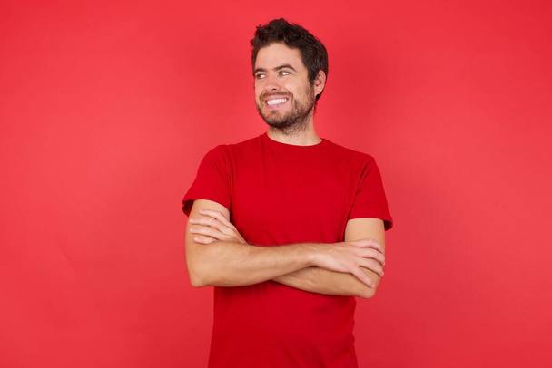 Blanke man met rood hemd in studio, armen over elkaar, glimlachend gelukkig  - Foto, afbeelding