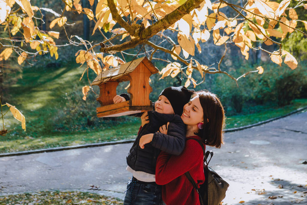 Молодая мать с маленьким ребенком положила семена в кормушку для птиц. осень - Фото, изображение