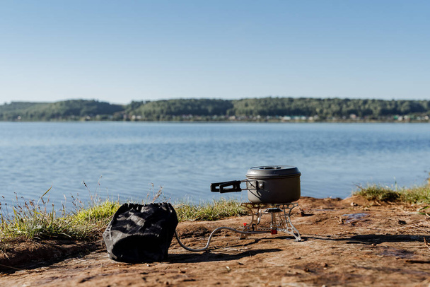 cooking on a gas burner in nature, gas camping stove for cooking food, aluminum pot with a lid stands on the burner, camping equipment for cooking. - 写真・画像