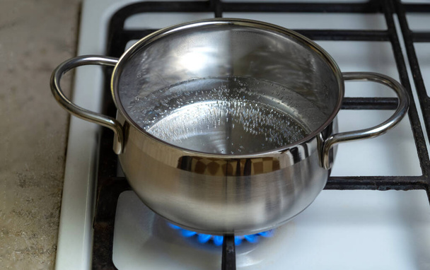 A água em uma panela de aço inoxidável é aquecida em um fogão a gás. - Foto, Imagem