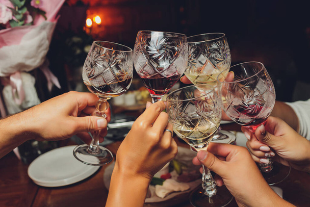 ボケの背景の前でワインやシャンパンでグラスをクリックしている人々のグループのショットを閉じます。高齢者の手. - 写真・画像