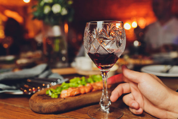 Adult hand holding glass of red whine. Toasting at celebration . Cafe or restaurant background. Chief speech while corporate business party. - 写真・画像