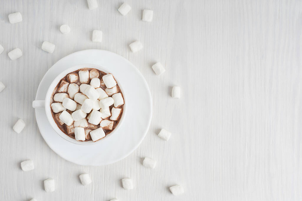 View from above on cup full of sweet homemade cacao drink usually prepared at cold winter holidays served on plate with marshmallows on white wooden background. Image with copy space, horizontal - Photo, image