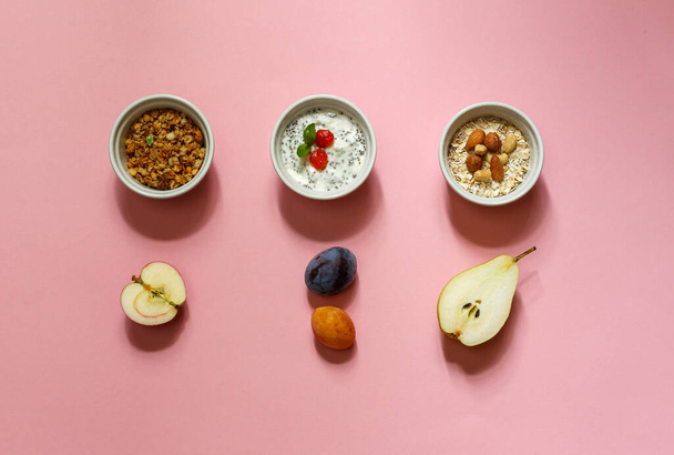 gesundes Frühstücksset mit Müsli, Haferflocken, Joghurt und Obst. Layout auf rosa Hintergrund horizontal - Foto, Bild