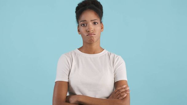 Portret van gefrustreerd Afrikaans Amerikaans meisje met armen gekruist droevig kijkend in camera over blauwe achtergrond - Foto, afbeelding