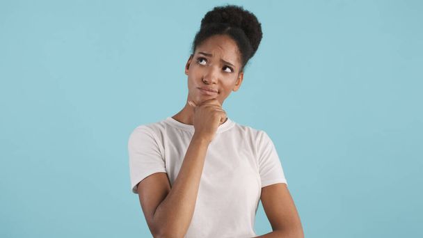 Portrét zamyšlené afroamerické dívky držící ruku na bradě zamyšleně hledící přes pestrobarevné pozadí. Hluboko v myšlenkách výraz - Fotografie, Obrázek