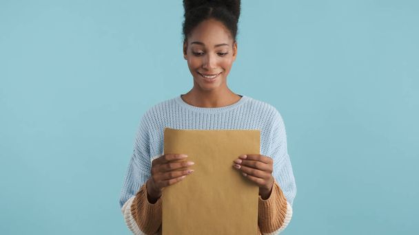 Atractiva sonrisa afroamericana chica americana abriendo sobre con los resultados de los exámenes en la cámara sobre fondo colorido - Foto, imagen