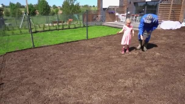 Father and little helper daughter seeding sowing lawn in yard. Handheld shot - Footage, Video