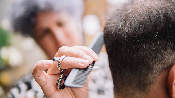 Photo d'un homme méconnu avec une grosse barbe blanche se faisant couper les cheveux. Le coiffeur utilise un peigne et les ciseaux. - Photo, image