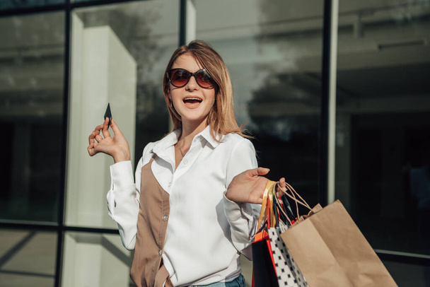 Portrait of european lady hold hand colorful bags woman after shopping in sunglasses white shirt jeans retail store near mall on the street sales black friday season bokeh background - Foto, afbeelding
